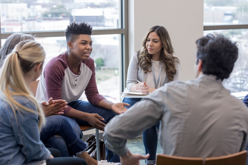 As the therapy group members listen, the teen boy shares his life experiences.